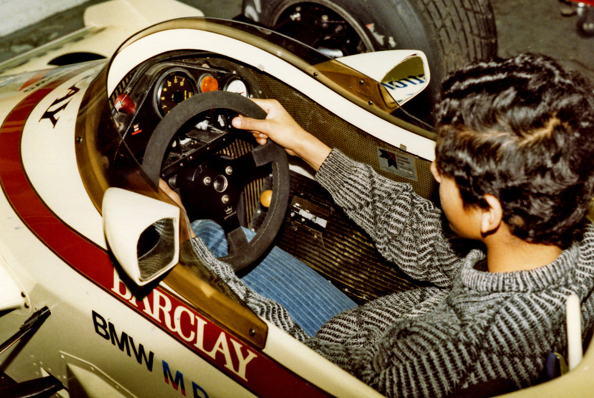 Young Capramont founder seated in a racing-car cockpit during the same private visit around 1985